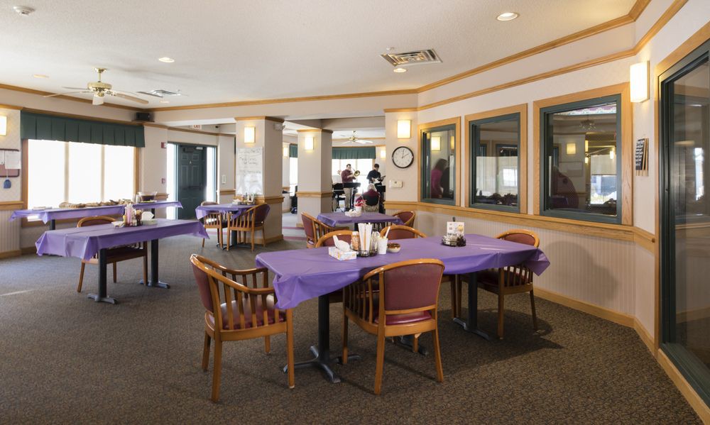 A spacious dining area with tables covered in purple tablecloths and wooden chairs.