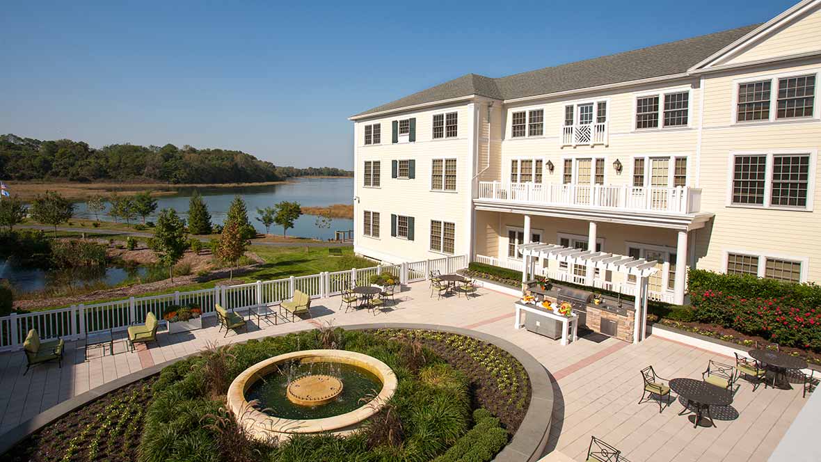 A scenic view of a hotel with a patio overlooking a lake and garden.