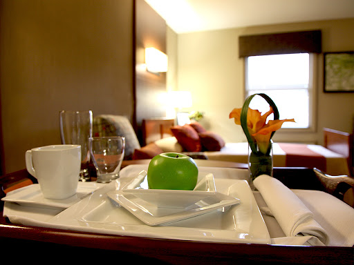 A neatly arranged hotel room service tray featuring a green apple and a floral centerpiece.