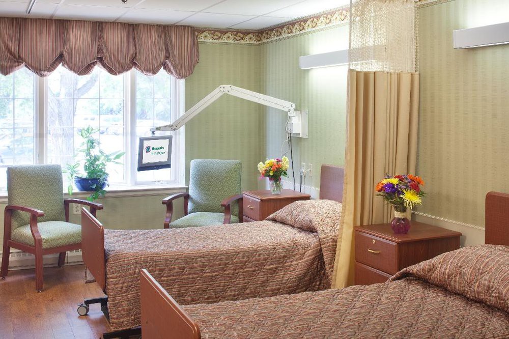 A hospital room with two beds, separated by a curtain, and decorated with flowers.