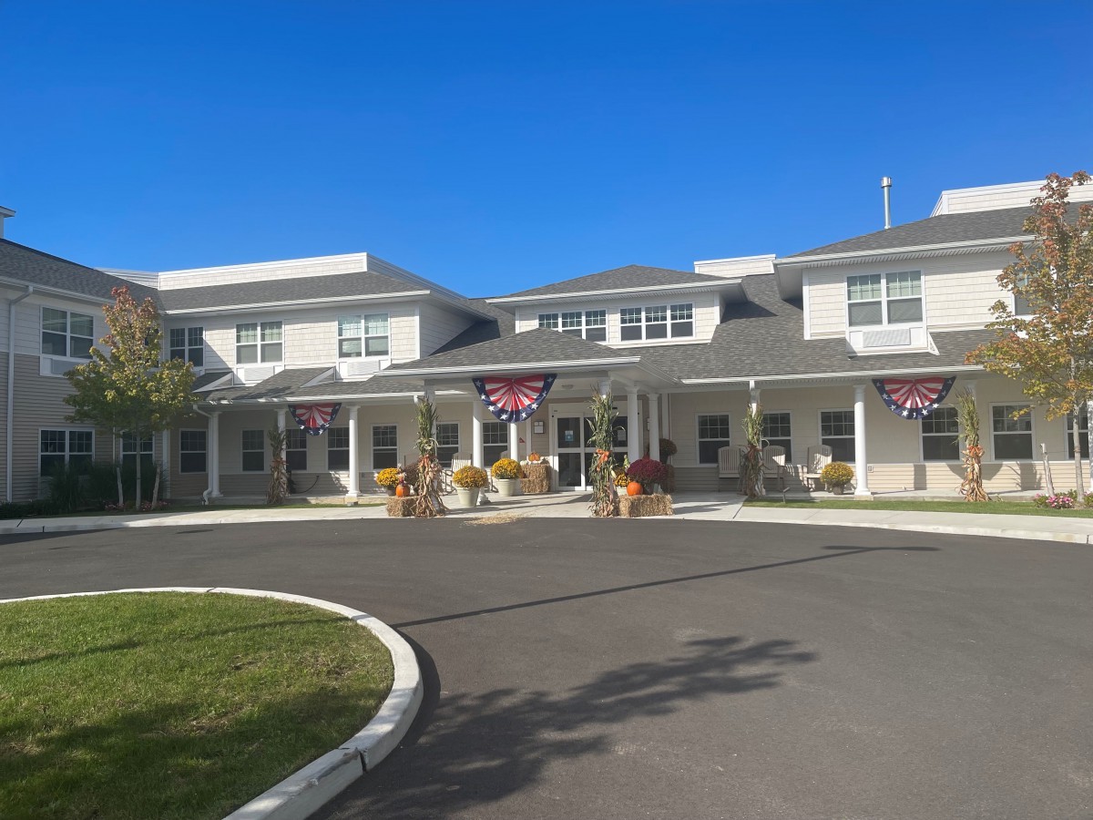 A building with an entrance and driveway, adorned with flags and surrounded by landscaping.