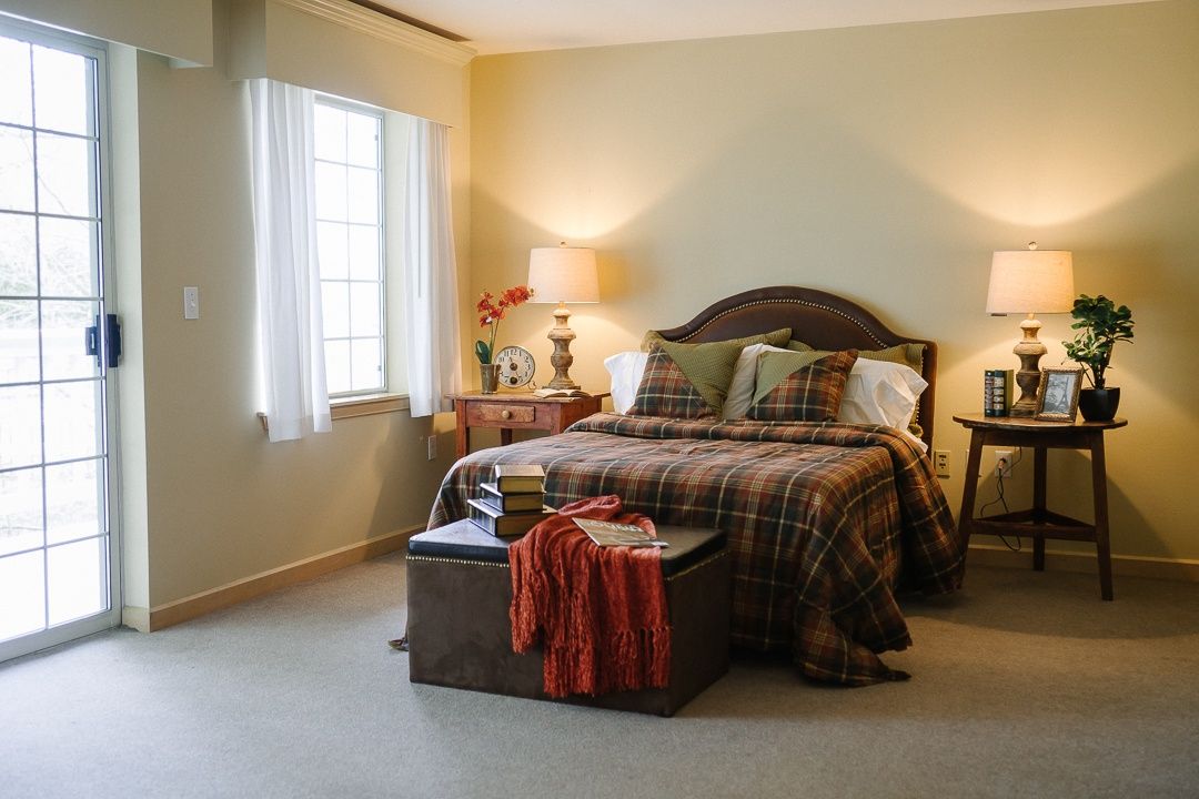A cozy bedroom with a neatly made bed, side tables with lamps, and a window letting in natural light.