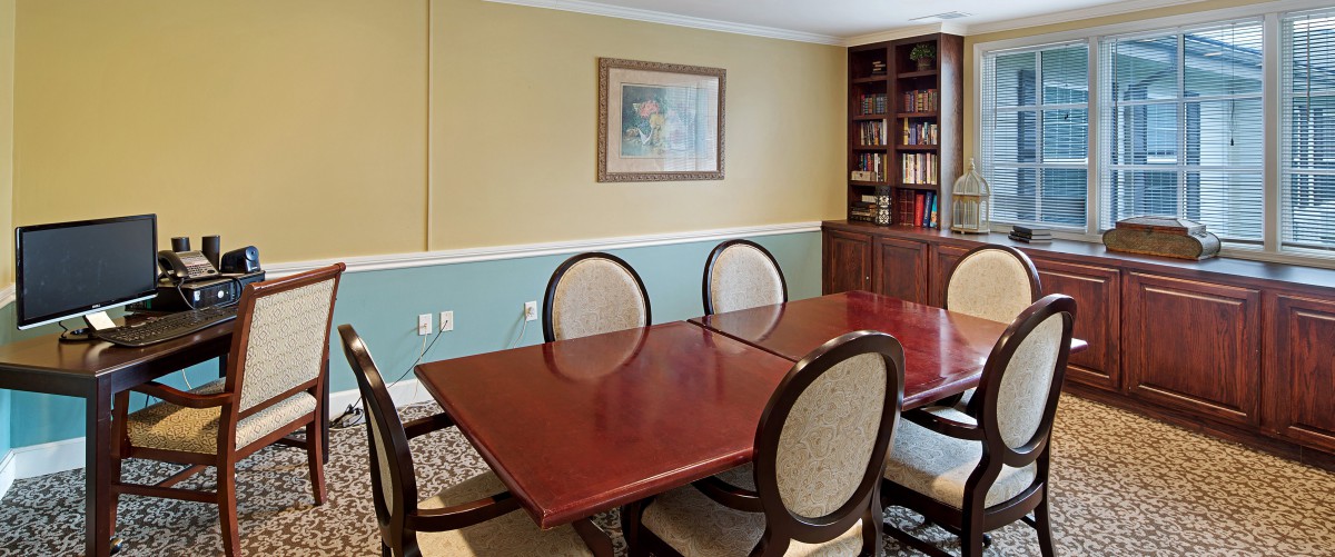A dining room with a wooden table, four upholstered chairs, a bookshelf filled with books, and artwork on the wall.