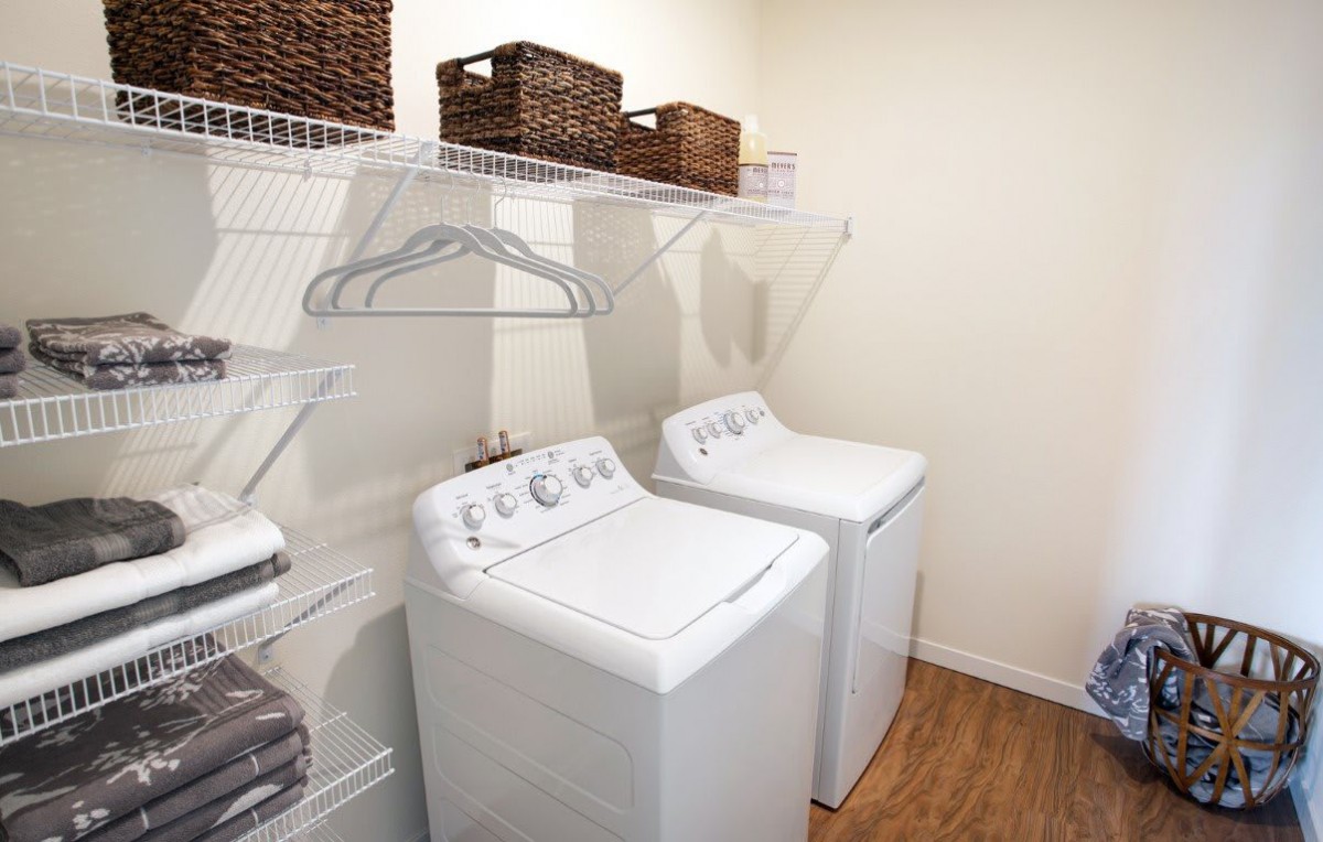 A neatly organized laundry room featuring a washer and dryer, with shelves containing storage baskets and hangers.