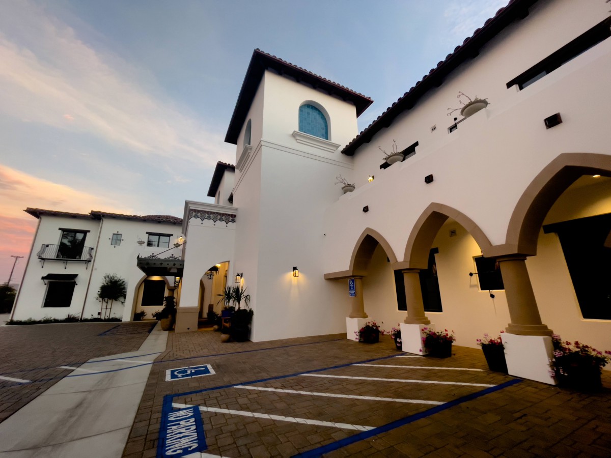 A Spanish-style building with arched doorways and a parking lot at sunset.