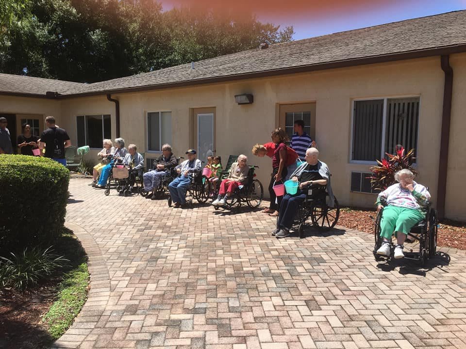 A group of elderly individuals sitting in wheelchairs outside on a sunny day.