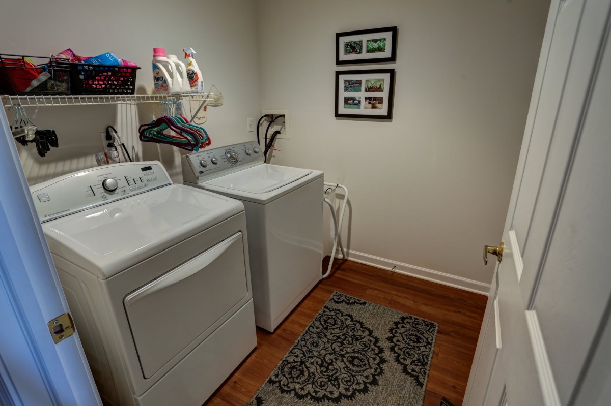 A tidy laundry room featuring a washer and dryer, with shelving for storage and framed pictures on the wall.