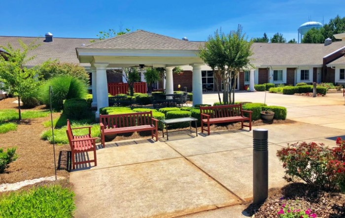 A sunny outdoor area with benches, shrubbery, and a building entrance.