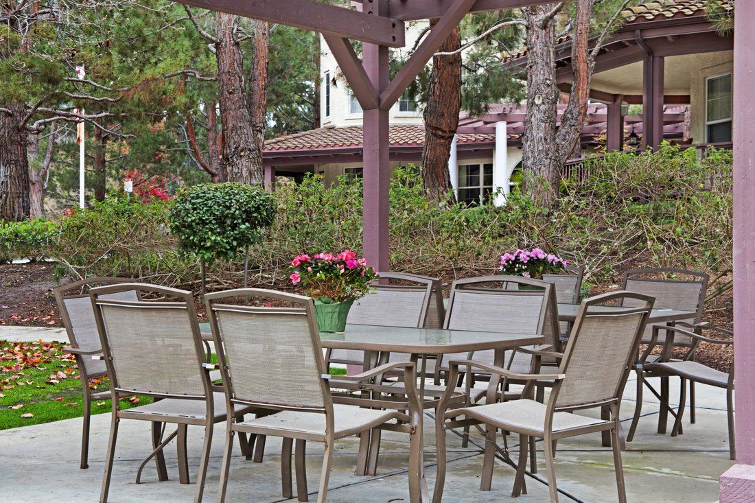 A cozy outdoor patio setup with tables and chairs under a pergola, surrounded by greenery and flowers.