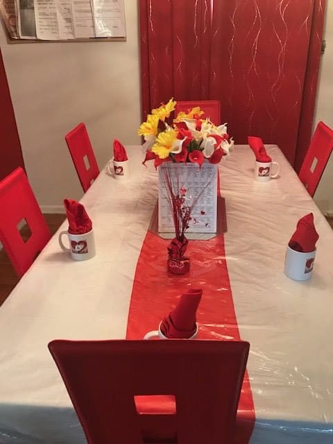 A beautifully set dining table with a red and white theme, featuring a central flower arrangement and creatively folded napkins in mugs.