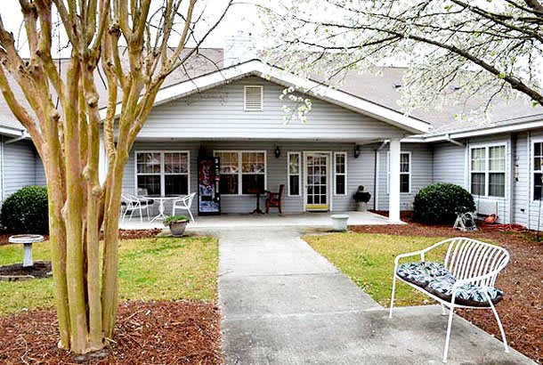 A welcoming residential home with a porch, surrounded by a well-maintained front yard and benches along the pathway.