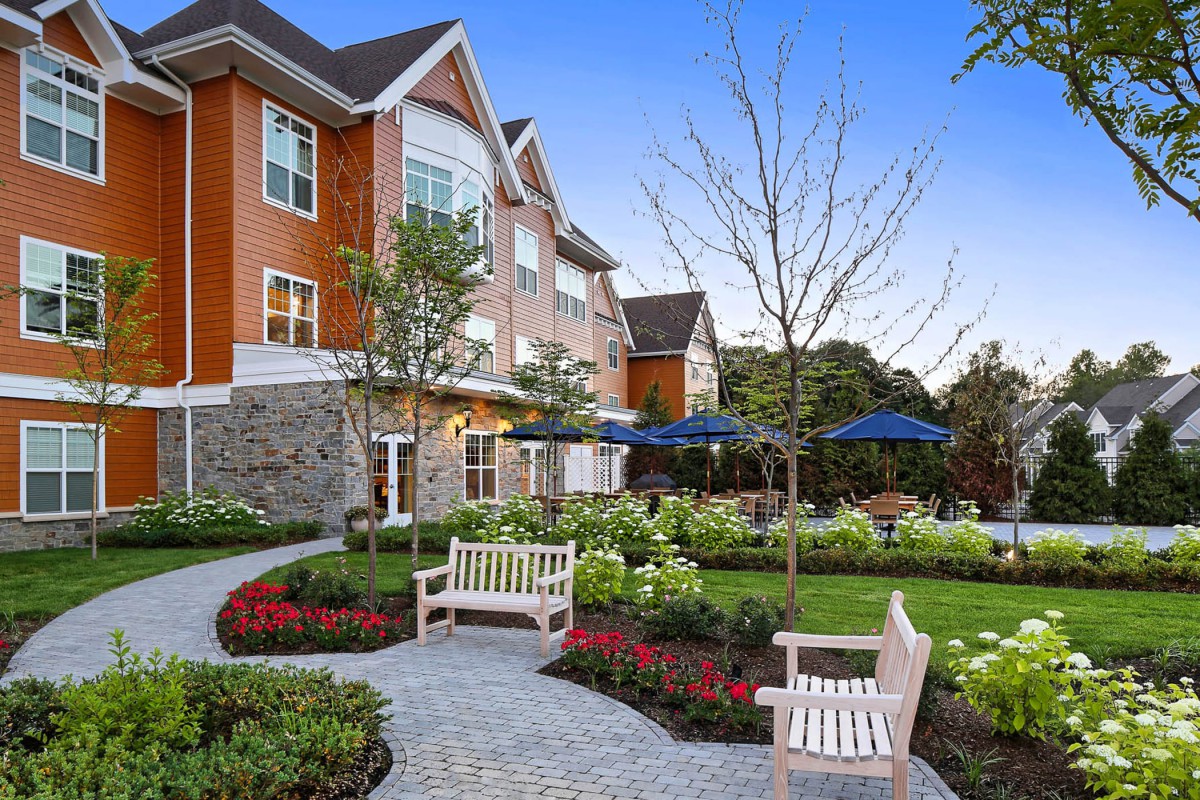 A beautifully landscaped garden with benches and a pathway in front of a residential building.