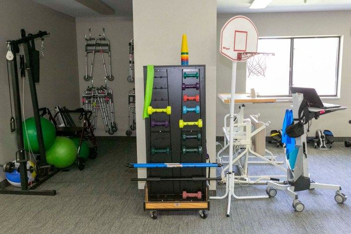 A physical therapy room featuring exercise equipment such as weights and resistance bands, along with a basketball hoop for rehabilitation exercises.