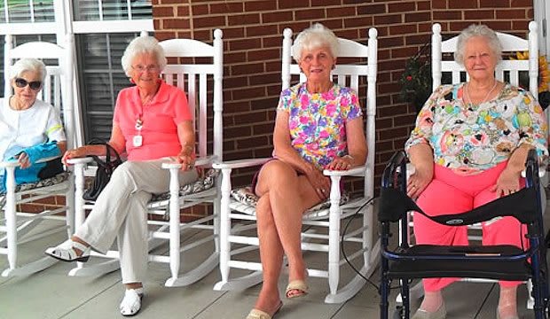 Elderly women sitting on rocking chairs on a porch, enjoying a summer day.