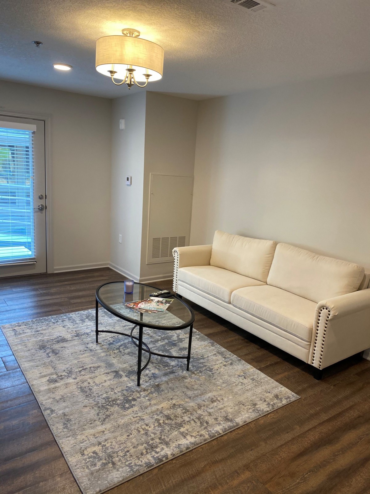 A minimalist living room featuring a white couch, glass-top coffee table, and a patterned rug on wooden flooring.