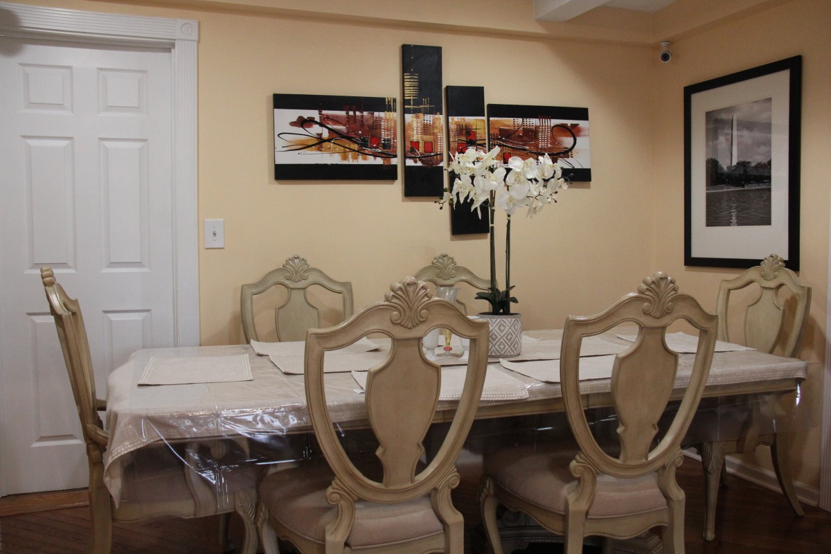 A beautifully decorated dining room with elegant chairs, a large table, and a centerpiece of white orchids under decorative wall art.