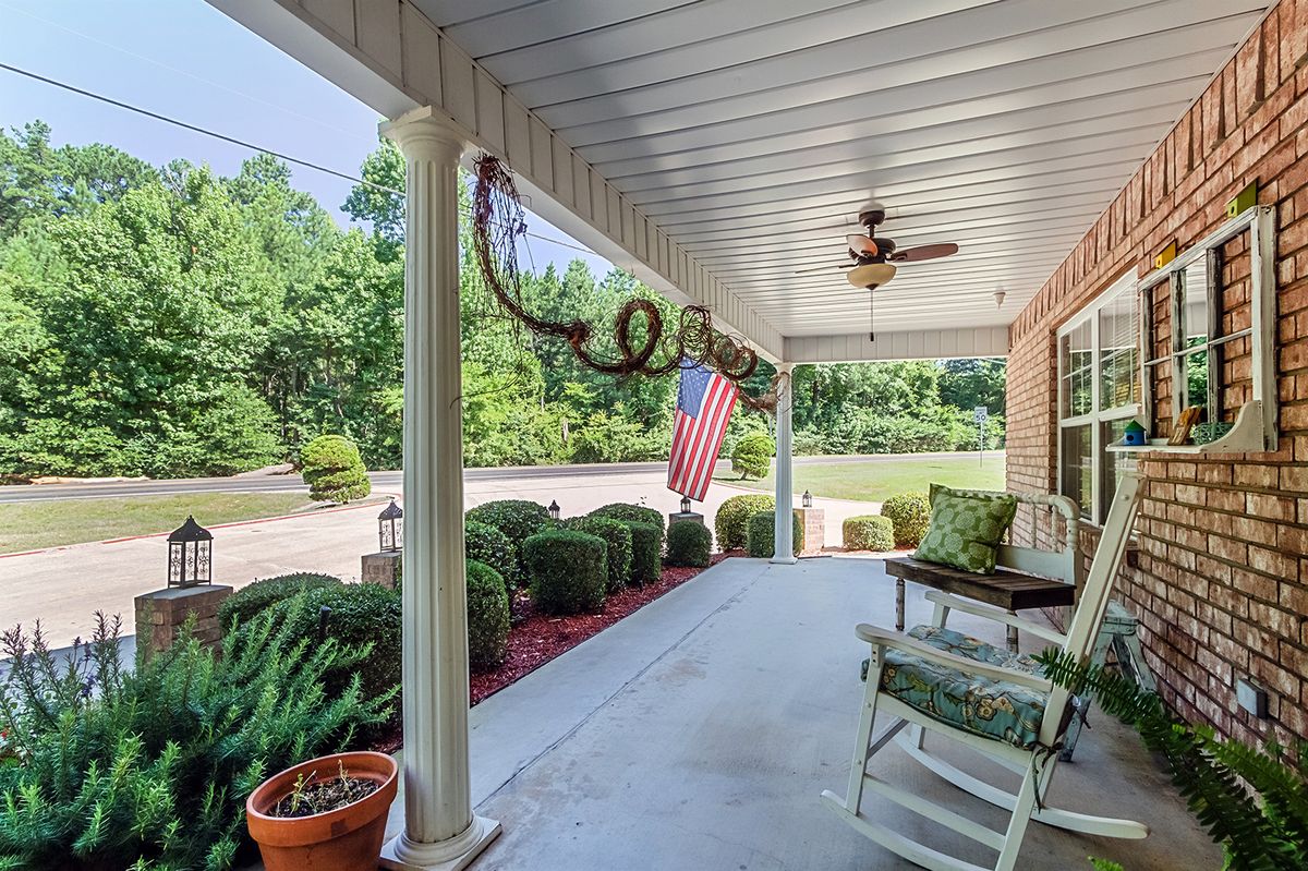 A cozy porch with rocking chairs and an American flag, surrounded by lush greenery.