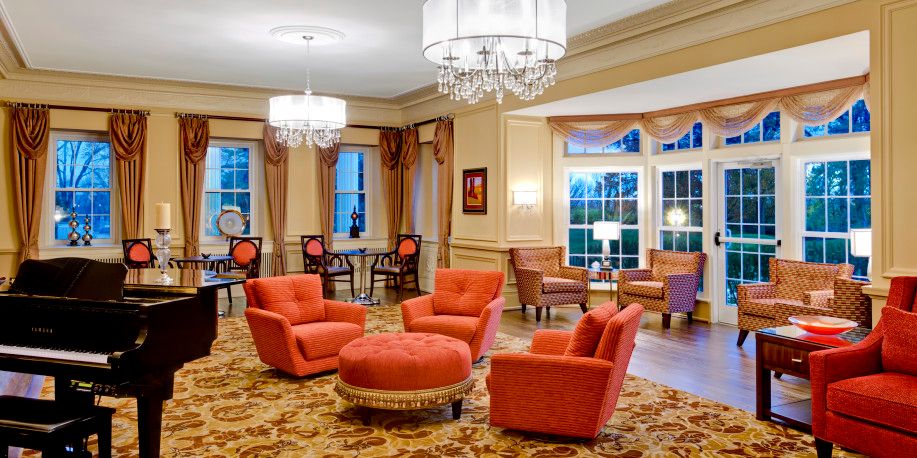 A luxurious lounge area featuring elegant chandeliers, plush armchairs, and a central ottoman in a warmly decorated room.