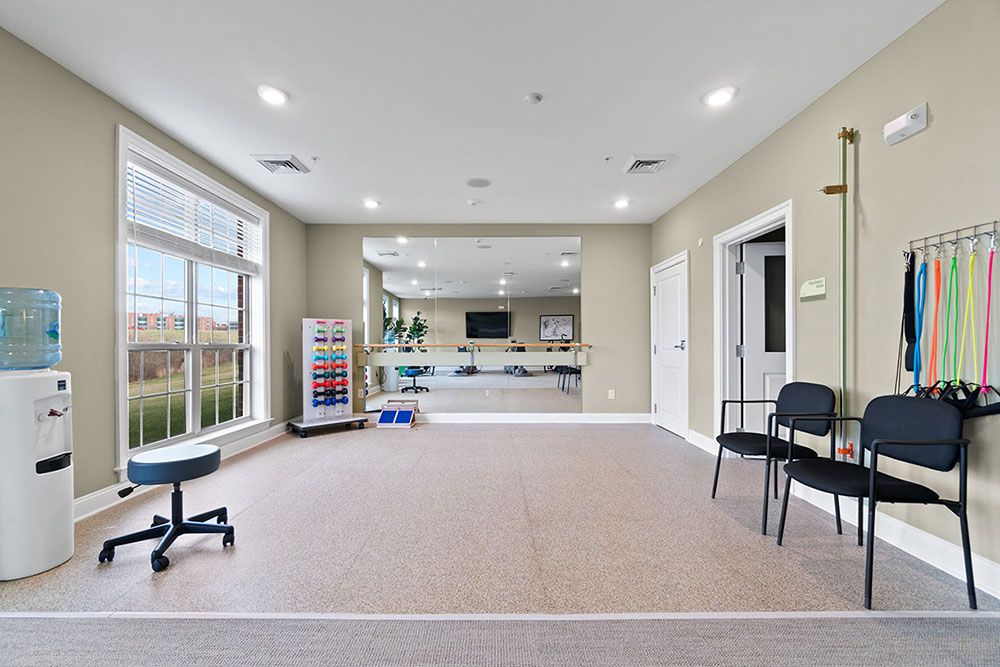 A spacious and well-lit room with chairs, a large mirror, and ample natural light coming through the windows.