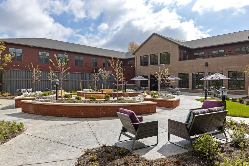 A well-designed courtyard area with outdoor seating and landscaping in front of a modern building under a partly cloudy sky.