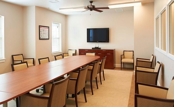 A modern conference room with a long table, multiple chairs, and a wall-mounted television.
