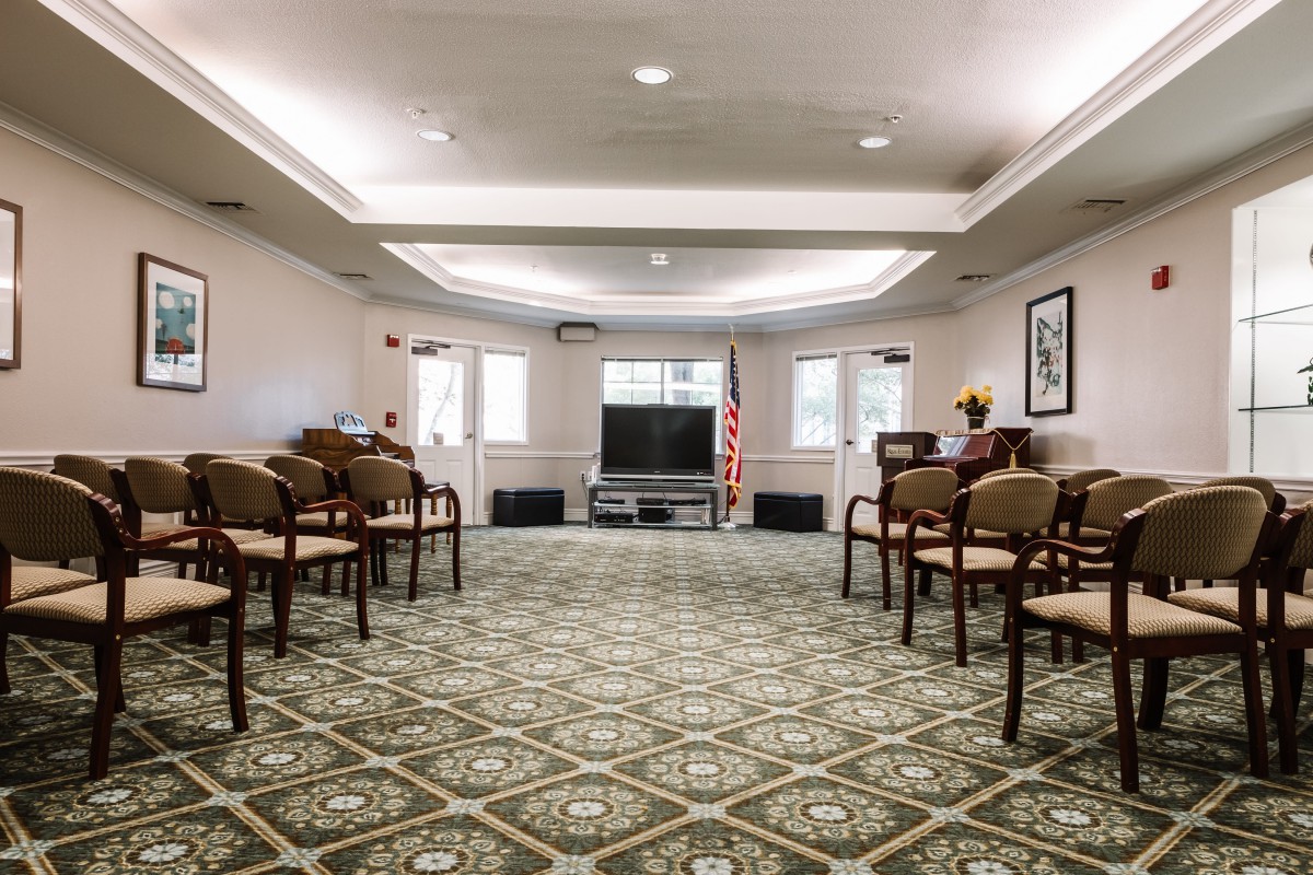 An empty conference room with arranged chairs, a television at the front, and an American flag.
