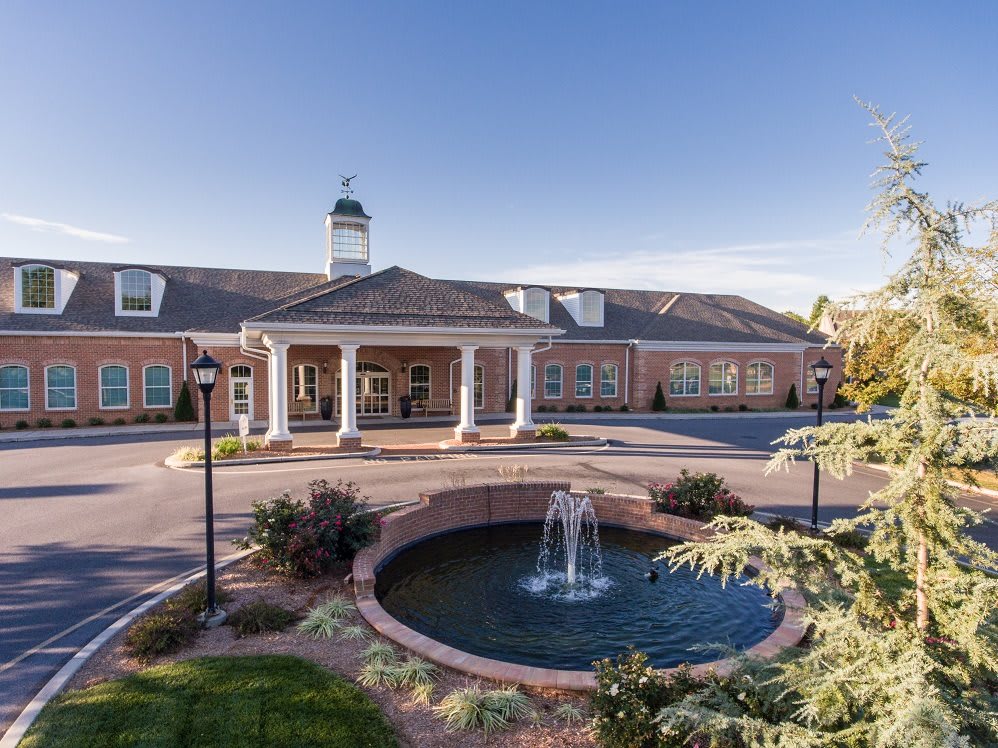 A stately brick building with a central fountain in the foreground, showcasing elegant architecture under a clear blue sky.