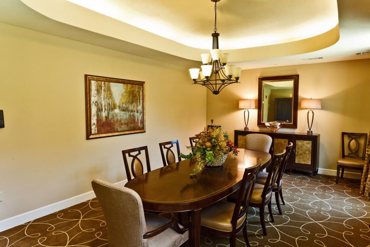A well-decorated dining room with an elegant chandelier hanging above a wooden table surrounded by chairs, complemented by wall art and a large mirror.