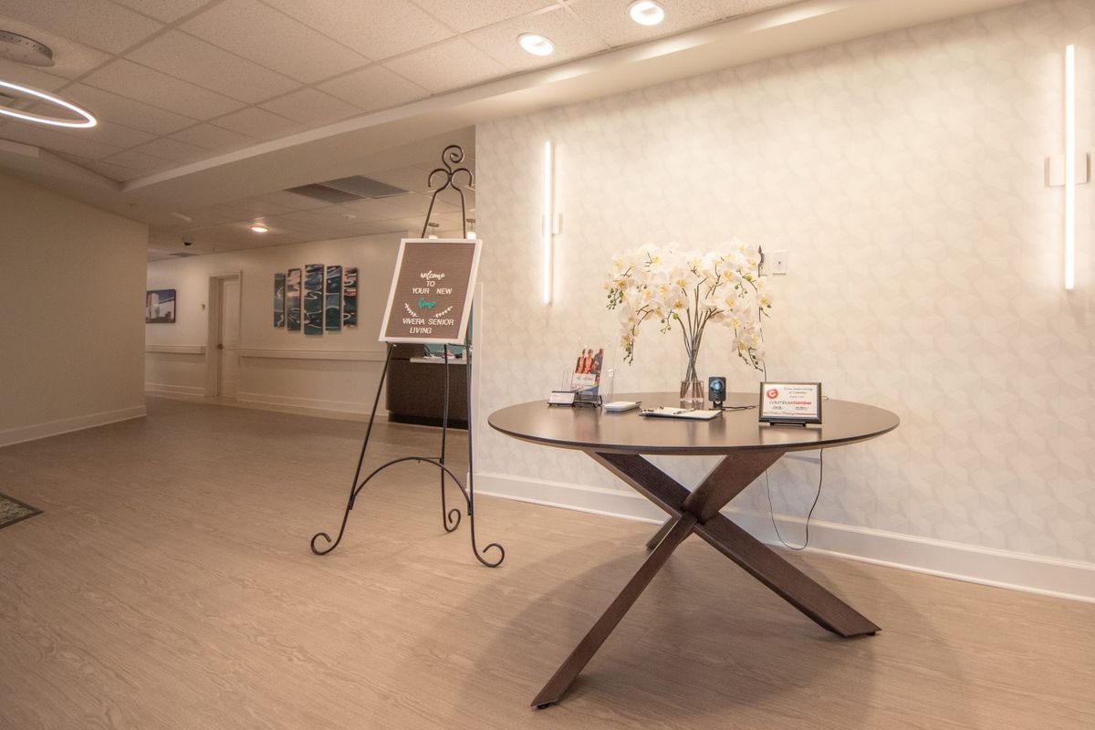 A well-lit lobby area featuring a round table with decorative flowers and a standing signboard.