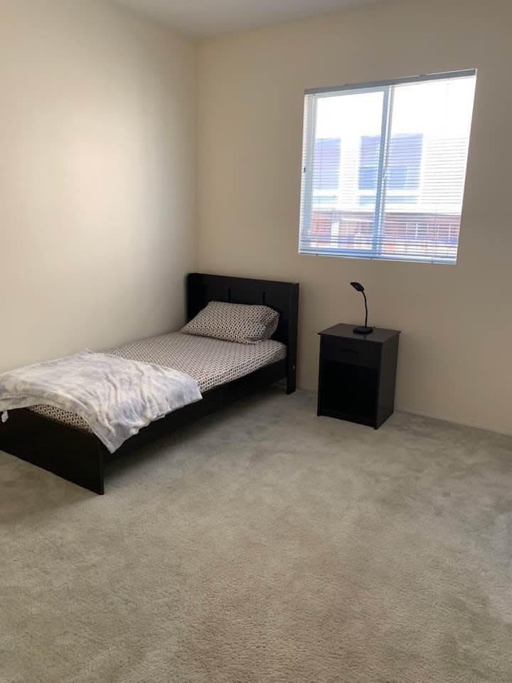 A minimalist bedroom with a single bed and nightstand near a window.