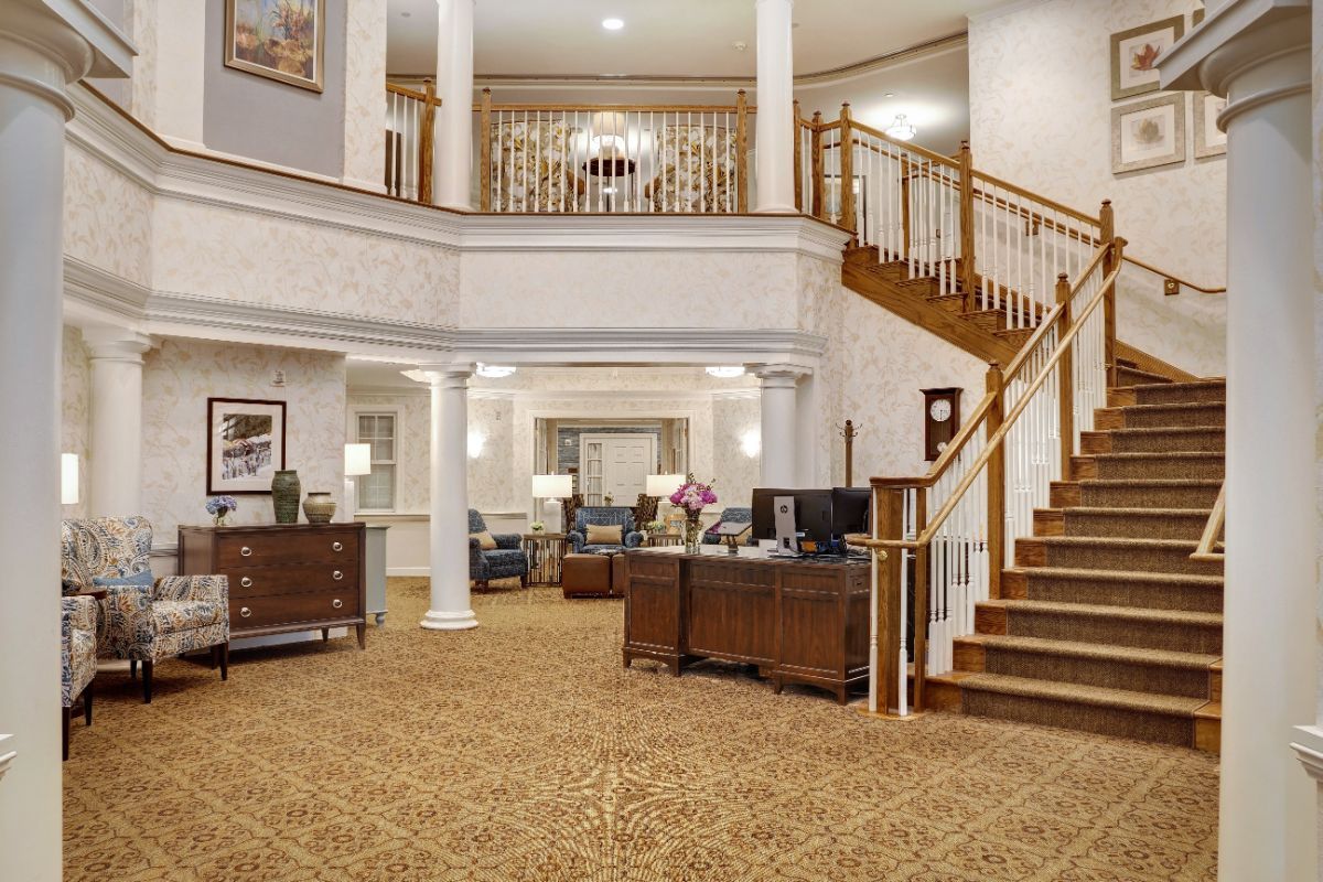 A spacious hotel lobby with elegant decor, featuring a grand staircase, reception desk, and comfortable seating.