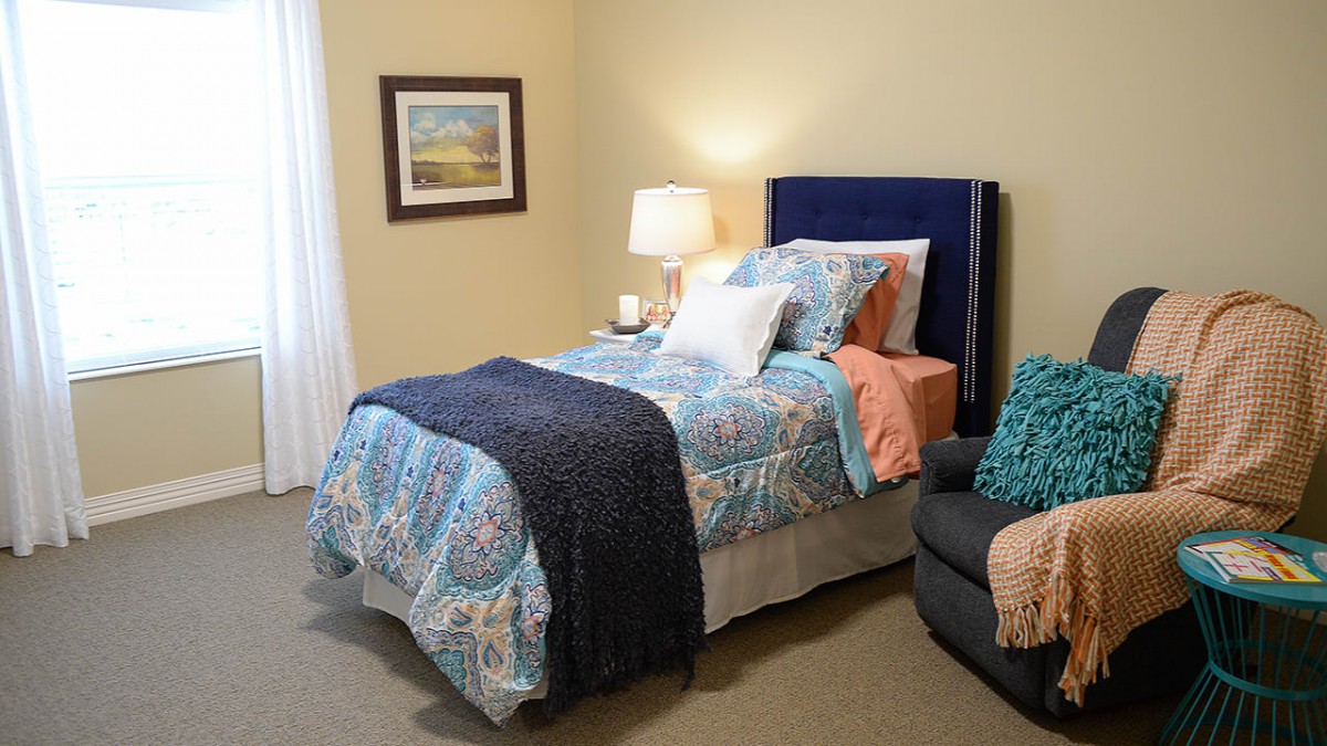 A cozy bedroom setup featuring a neatly made bed with colorful bedding and a lamp on the bedside table.