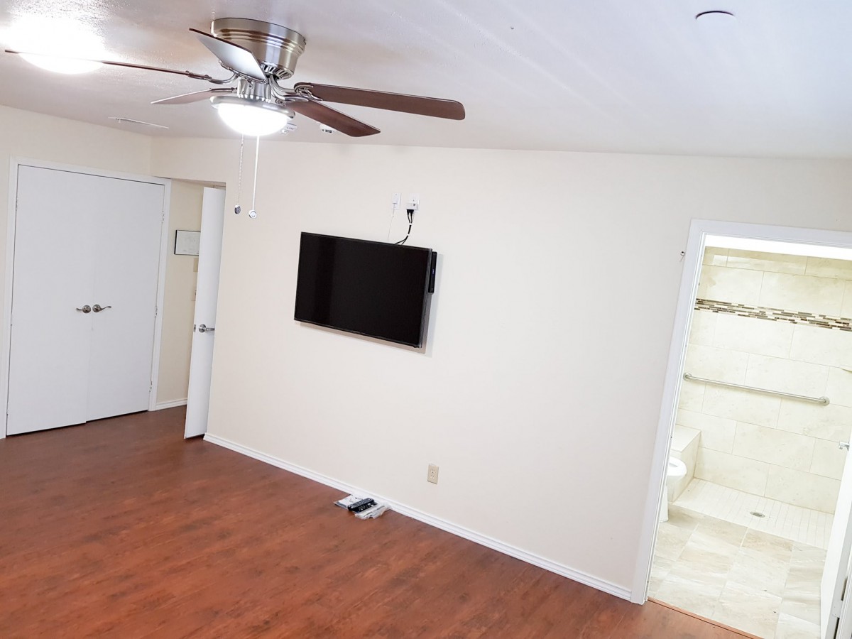 A living room with a ceiling fan, wall-mounted TV, and wooden floors.