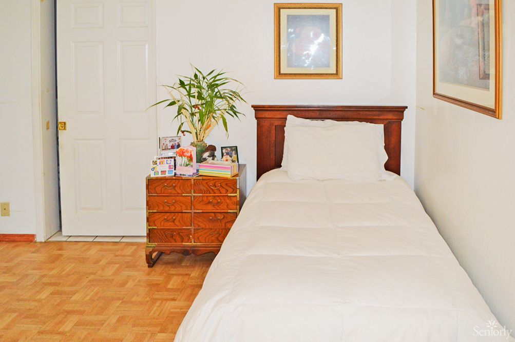 A cozy bedroom with a single bed and a wooden nightstand featuring decorative items and a potted plant.
