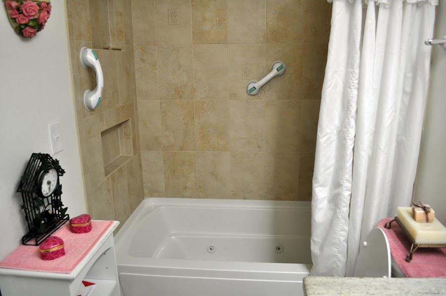 A bathroom featuring a bathtub with grab bars and a beige tiled wall.