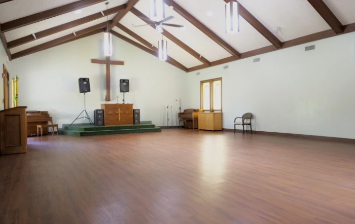 An empty church interior with a cross and altar on a wooden floor.