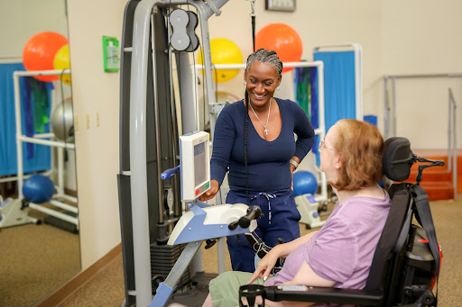 A healthcare professional assists a patient in a rehabilitation setting, demonstrating the use of exercise equipment.