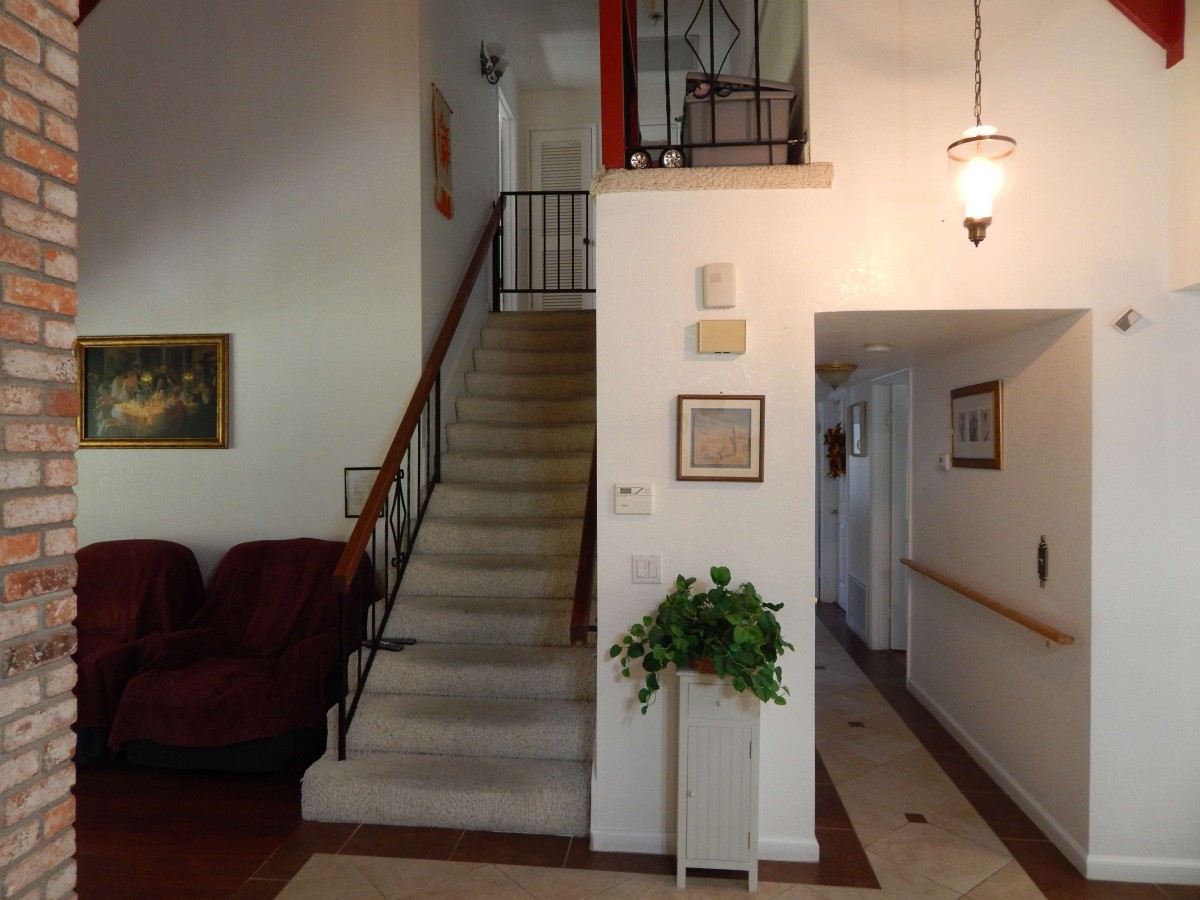 A cozy living room with a staircase leading to the upper floor, adorned with wall art and potted plants.
