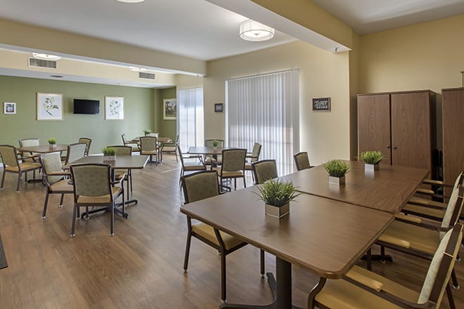 A modern dining area with neatly arranged tables and chairs, featuring decorative plants and ample natural light.