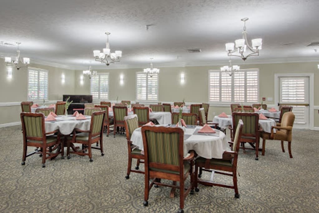 An elegantly arranged dining room with multiple tables and chairs, illuminated by chandeliers.