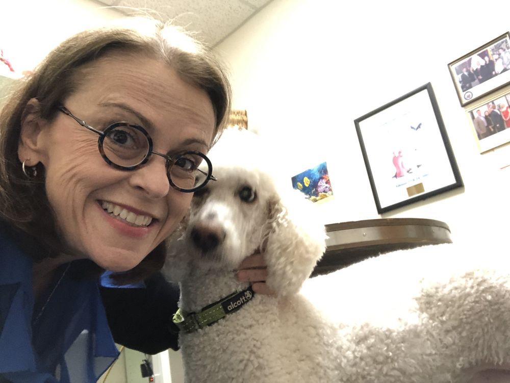 A woman wearing glasses takes a selfie with her dog indoors.