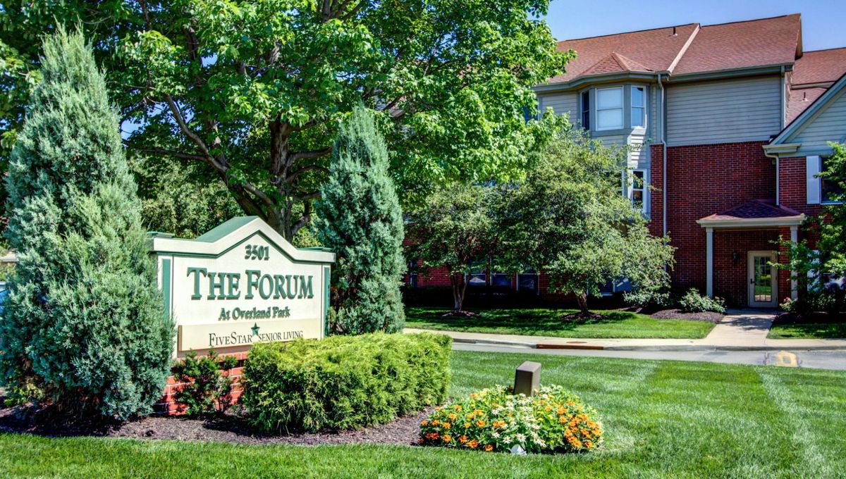 Entrance sign to The Forum apartment complex surrounded by lush greenery and well-maintained landscaping.