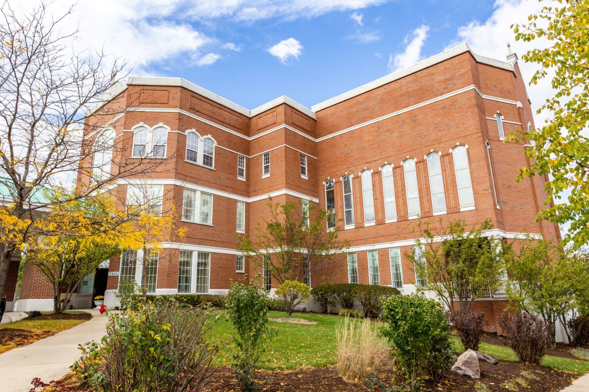 A red brick building surrounded by trees and landscaping under a partly cloudy sky.