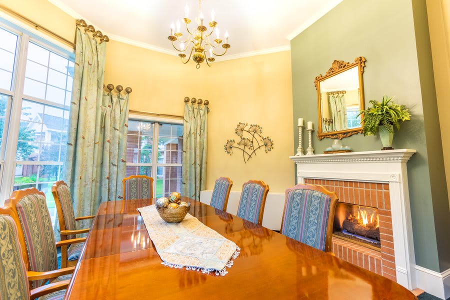 A cozy dining room with a polished wooden table, elegant chairs, and a warm fireplace.