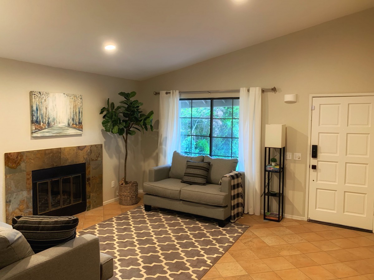 A cozy living room featuring a sofa, fireplace, and large window with curtains and a decorative rug.