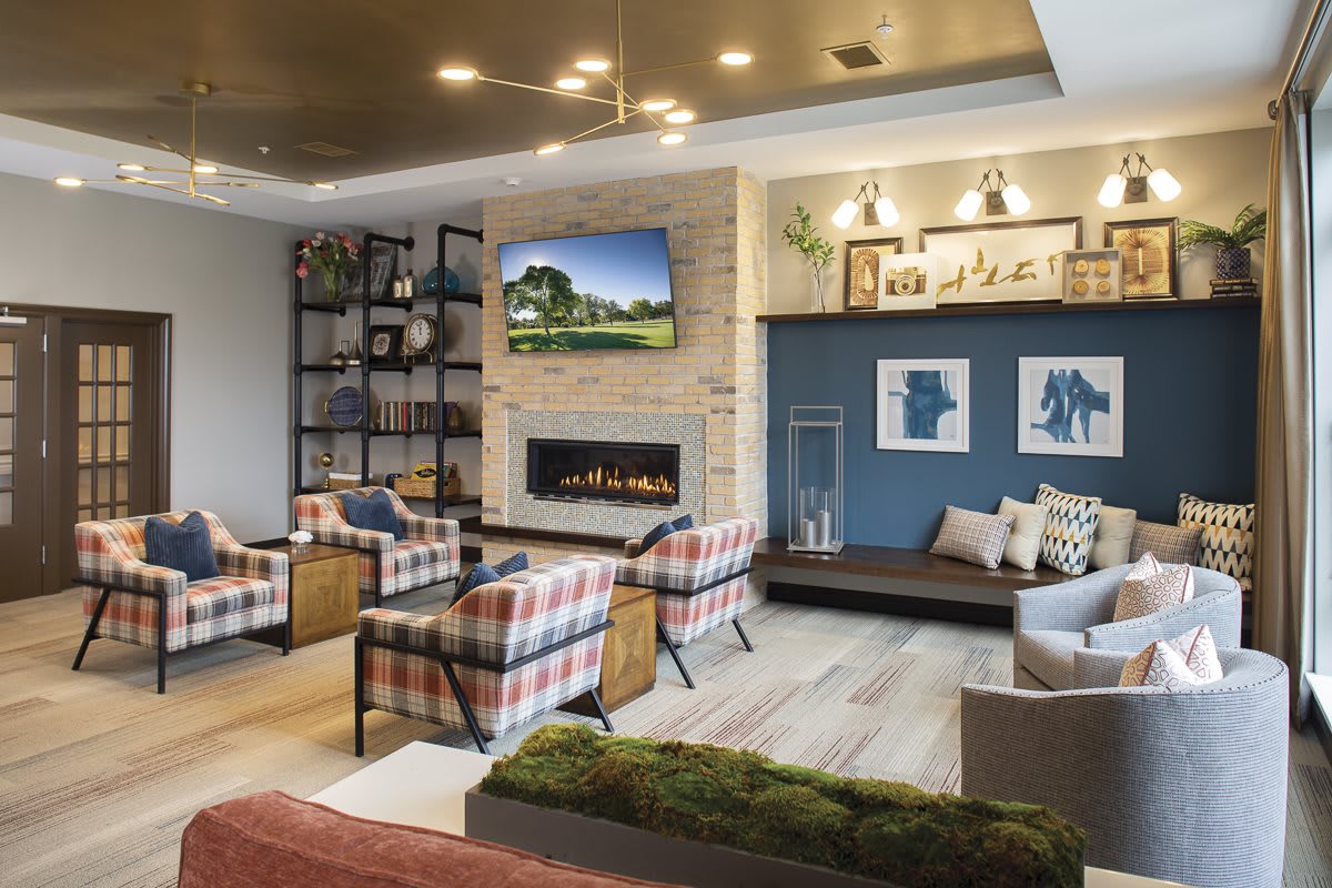 A cozy living room featuring a modern fireplace, plaid armchairs, and stylish shelving.