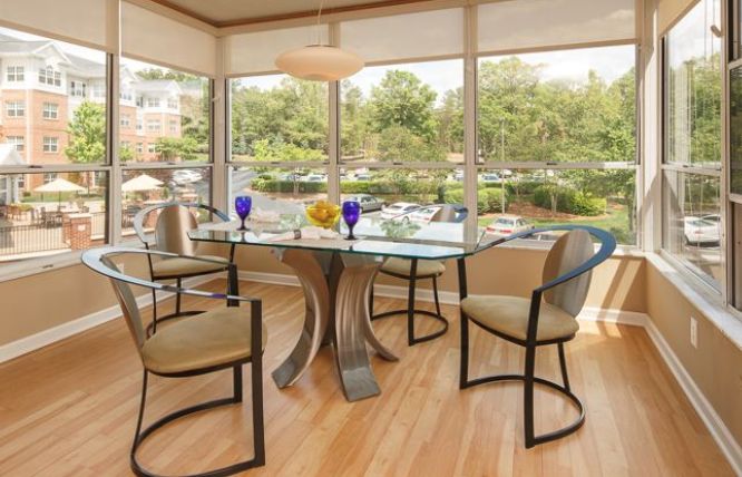 A modern dining room with a glass table and stylish chairs, surrounded by large windows that let in natural light.