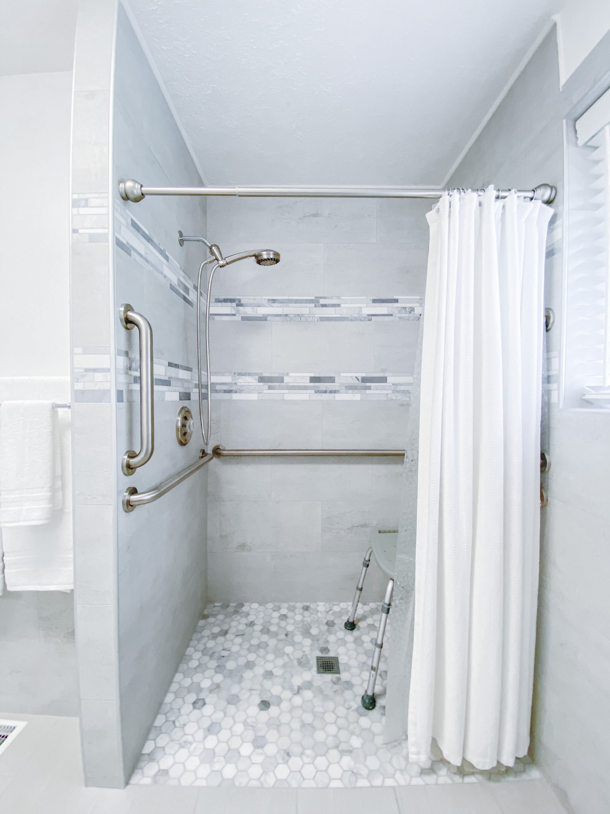 A modern bathroom shower area with marble flooring and grab bars.