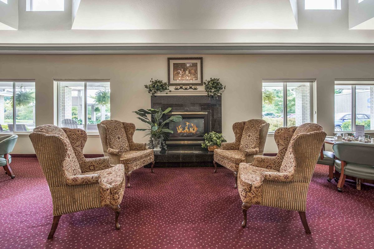 A cozy living room with elegant armchairs arranged around a fireplace, featuring decorative plants and artwork.