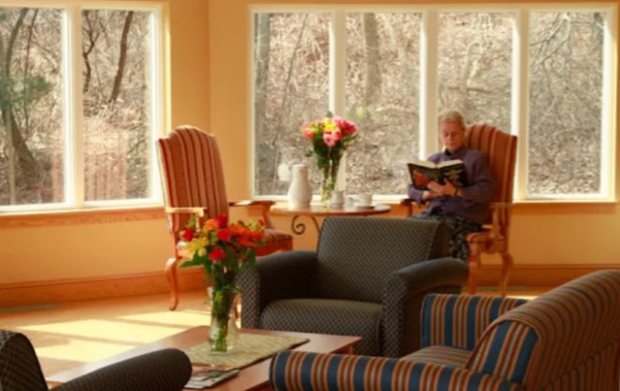 A cozy living room with comfortable seating, large windows overlooking the outdoors, and a person reading a book.